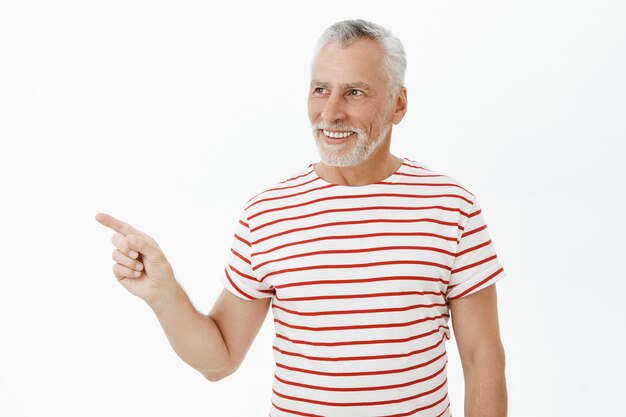 Pleased old man in t-shirt looking and pointing left