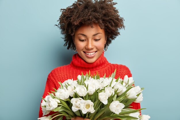 巻き毛の心地よい女性モデルが喜んで、白い春の花に幸せそうに見えます