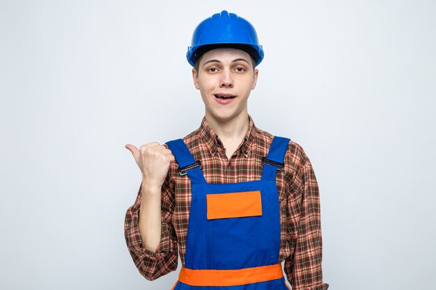 Pleased points at side young male builder wearing uniform 