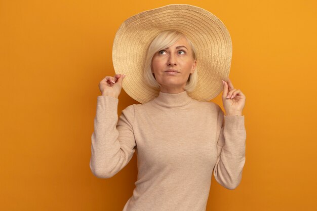 Довольная симпатичная славянская блондинка в пляжной шляпе смотрит на оранжевый