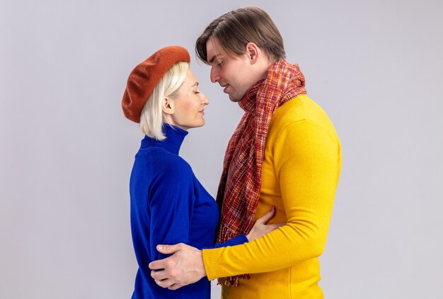 Довольная симпатичная блондинка в берете и красивый славянский мужчина с шарфом на шее смотрят друг на друга в день святого валентина