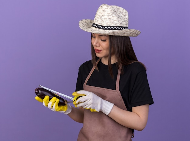 巻尺でナスを測定する園芸帽子と手袋を身に着けているかなり白人女性の庭師を喜ばせる
