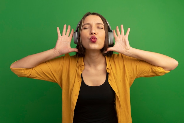 Free photo pleased pretty caucasian woman on headphones holds hands close to head on green