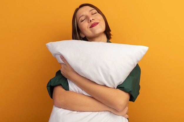 Free photo pleased pretty caucasian woman holds pillow on orange