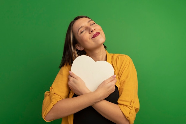 Free photo pleased pretty caucasian woman hugs heart shape on green