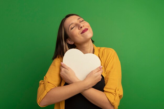 Pleased pretty caucasian woman hugs heart shape on green