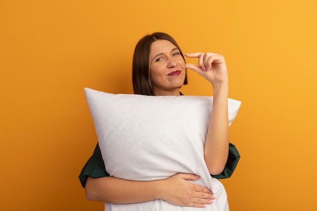 Pleased pretty caucasian woman hugs pillow and pretends to hold something on orange