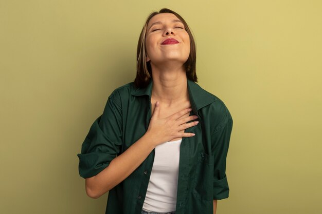 Pleased pretty caucasian woman puts hand on chest on olive green