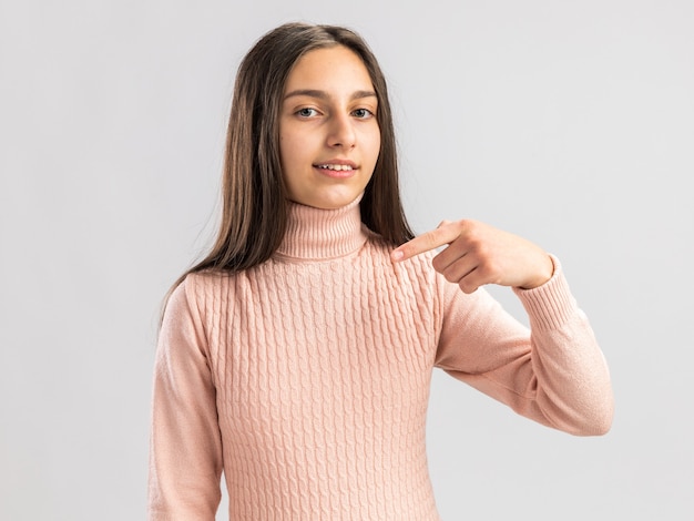 Pleased pretty teenage girl  pointing at space in front of her isolated on white wall