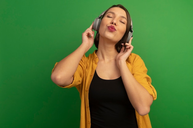 La bella donna soddisfatta sulle cuffie sta con gli occhi chiusi isolati sulla parete verde