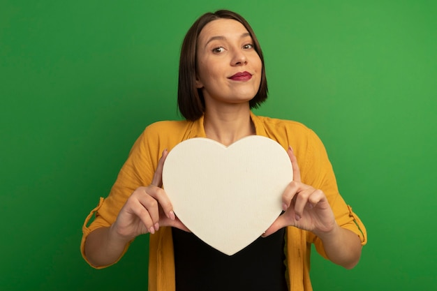 Foto gratuita la donna graziosa soddisfatta tiene la forma del cuore isolata sulla parete verde