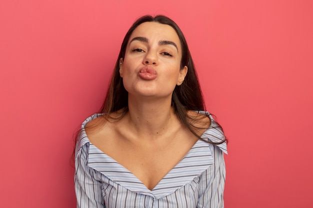 Pleased pretty woman pretends to kiss isolated on pink wall