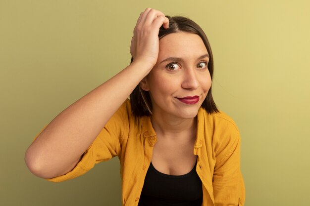 Pleased pretty woman puts hand on forehead isolated on olive green wall