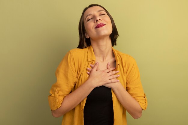 Pleased pretty woman puts hands on chest isolated on olive green wall