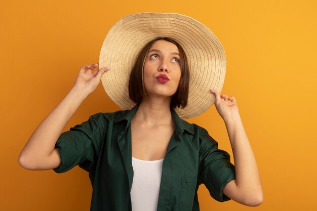 Pleased pretty woman with beach hat looks up isolated on orange wall