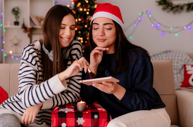 Pleased pretty young girls hold and look at powder palette sitting on armchairs and enjoying christmas time at home