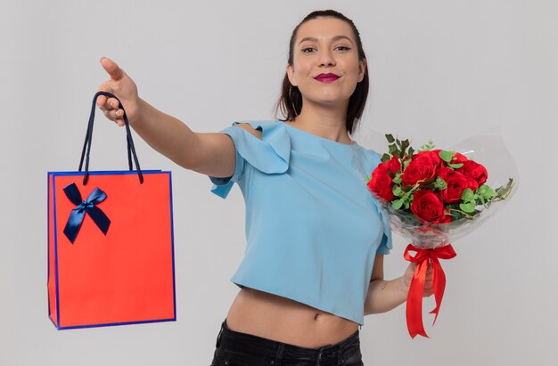 Pleased pretty young woman holding bouquet of flowers and gift bag looking at front