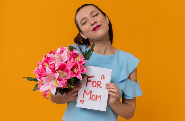 Pleased pretty young woman holding bouquet of flowers and letter from her child 