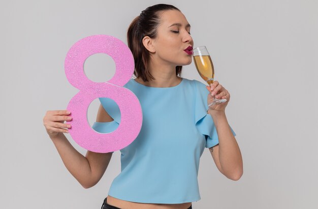 Довольная красивая молодая женщина держит розовый номер восемь и пьет шампанское