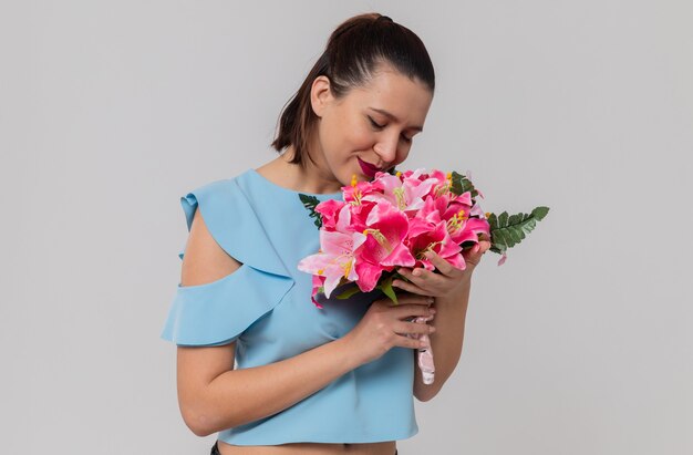 Pleased pretty young woman holding and sniffing bouquet of flowers