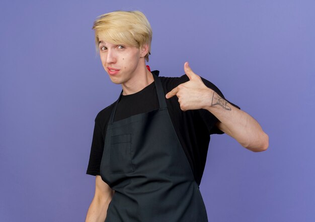 Free photo pleased professional barber man in apron pointing at himself feeling proud