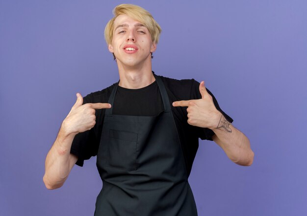 Pleased professional barber man in apron pointing at himself 