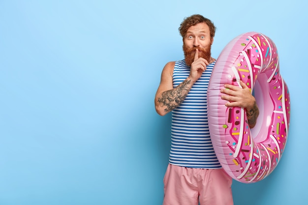 Pleased red haired man posing with donut pool floaty