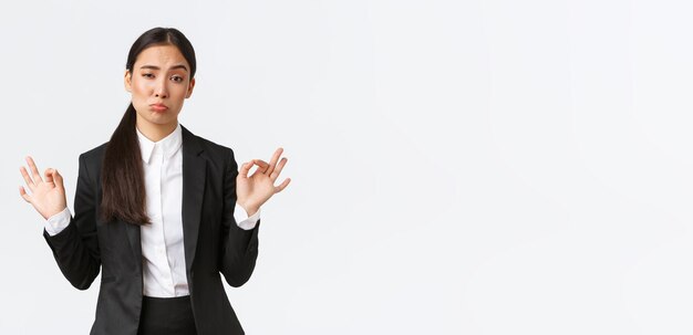 Pleased sassy asian businesswoman in black suit show not bad gesture nod in approval and make okay gesture very good work praising coworker standing satisfied over white background