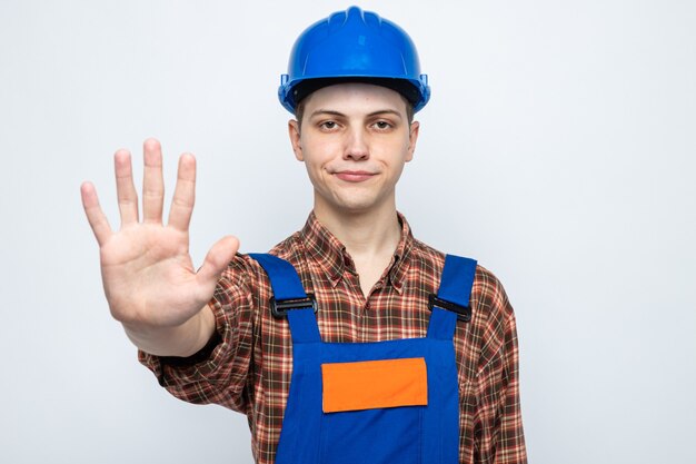 Pleased showing stop gesture young male builder wearing uniform 