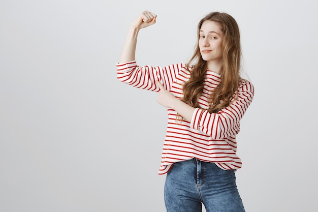 Free photo pleased teenage girl flex biceps and smirk satisfied