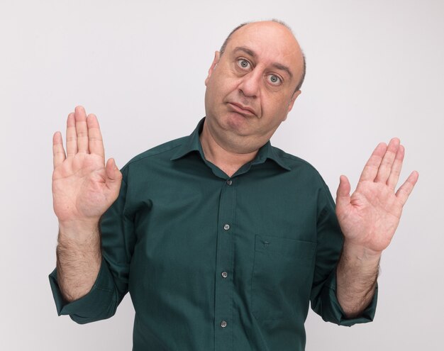 pleased tilting head middle-aged man wearing green t-shirt showing stop gesture isolated on white wall