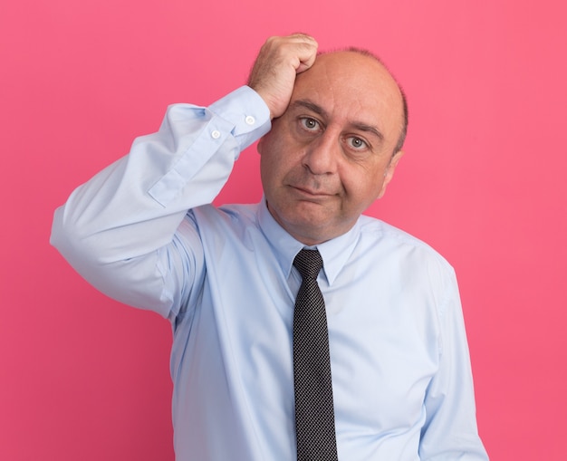 Pleased tilting head middle-aged man wearing white t-shirt with tie putting hand on head isolated on pink wall