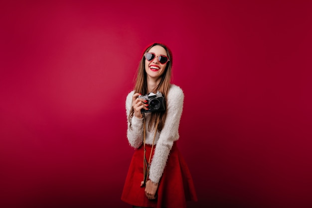 Pleased white girl in funny sunglasses holding camera and laughing