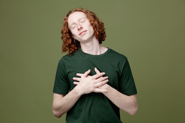 Free photo pleased with closed eyes putting hands on heart young handsome guy wearing green t shirt isolated on green background