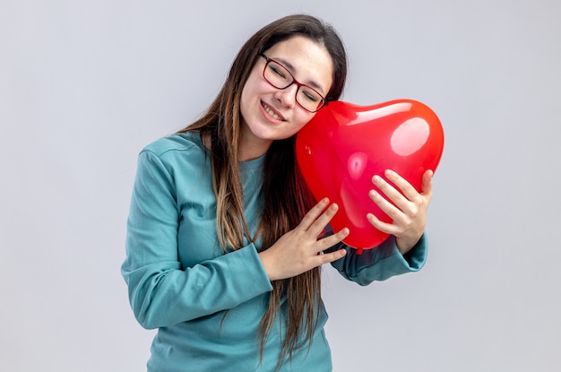 Pleased with closed eyes tilting head young girl on valentines day holding heart balloon isolated on white background