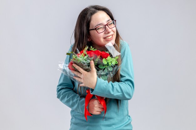 Pleased with closed eyes young girl on valentines day holding bouquet isolated on white background