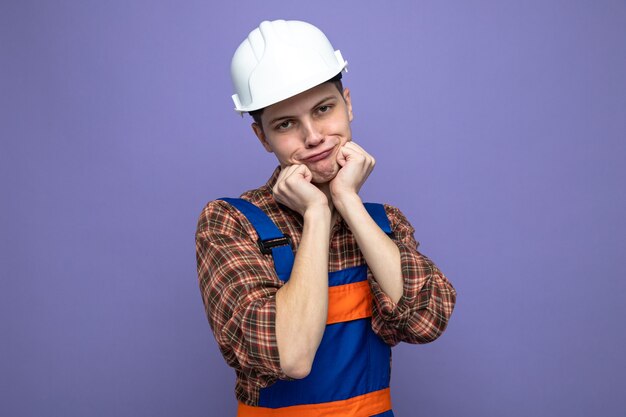 Soddisfatto delle mani intorno al viso giovane costruttore maschio che indossa l'uniforme