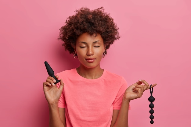 Pleased woman poses with anal beads, butt plug used to enchance climax, for pleasurable feelings in anus, achieves sexual pleasure with help of sex toys. Erotic stimulation focused on anus and rectum