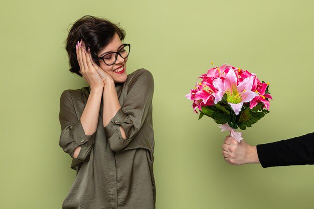 Pleased woman with short hair looking surprised and happy smiling cheerfully while receiving bouquet of flowers from her boyfriend celebrating international  women's day march 8