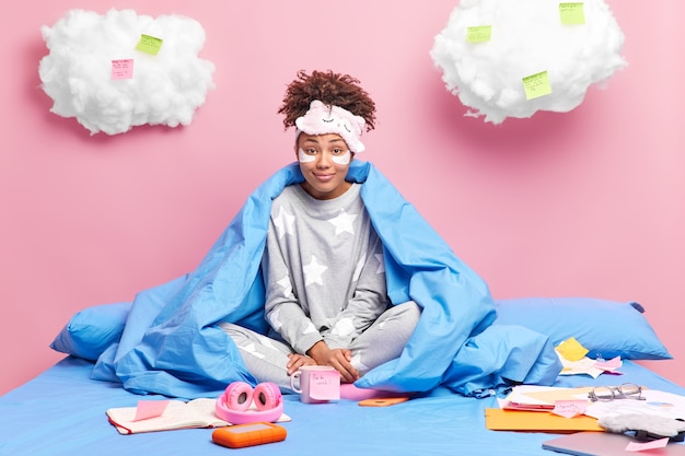 Pleased young African American college student does homework in bed at home