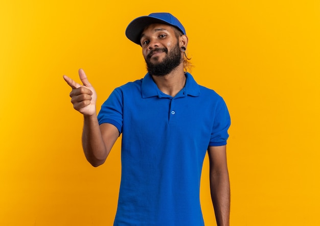 Pleased young afro-american delivery man pointing at side isolated on orange wall with copy space