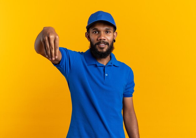 Pleased young afro-american delivery man pretending to hold something isolated on orange wall with copy space