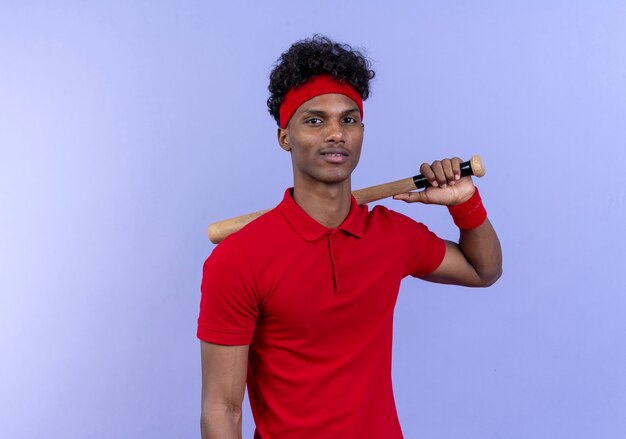 Довольный молодой афро-американский спортивный мужчина с повязкой на голову и браслет держит руку на плече изолированной на синей стене