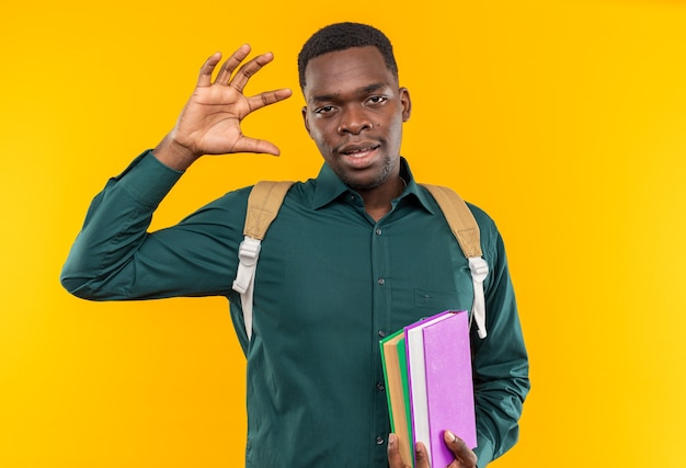 Pleased young afro-american student with backpack holding books and raising hand up 
