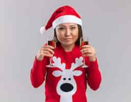 Free photo pleased young asian girl wearing christmas hat with sweater holding glass of champagne isolated on white background