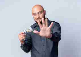 Free photo pleased young bald call center man holding money and stretching out hand towards camera isolated on white background