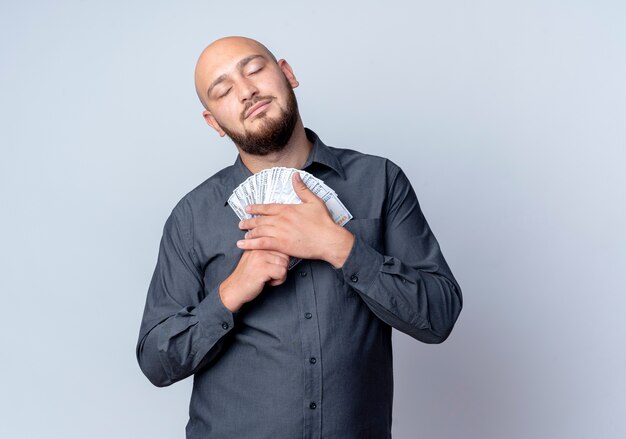 Pleased young bald call center man holding money with closed eyes isolated on white background with copy space
