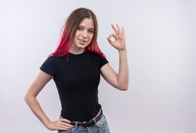 Pleased young beautiful girl wearing black t-shirt showing okay gesture putting her hand on hip on isolated white background with copy space