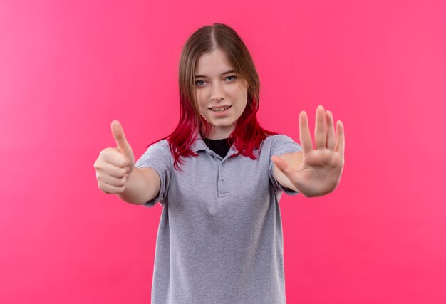 Довольная молодая красивая девушка в серой футболке показывает разные жесты на изолированном розовом фоне