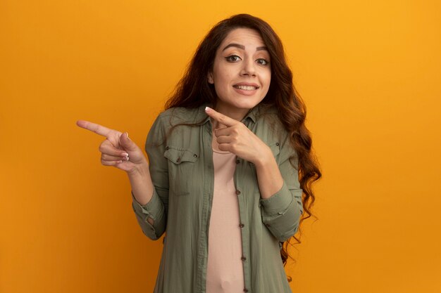 Pleased young beautiful girl wearing olive green t-shirt points at side isolated on yellow wall with copy space